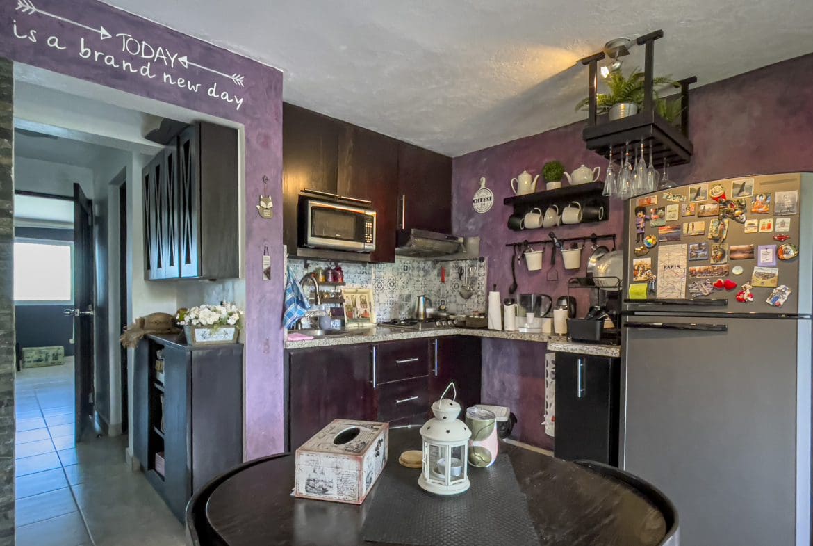 buyDRproperty Cozy kitchen with dark cabinets, microwave, and refrigerator. "Today is a brand new day" sign. Sosua Real Estate