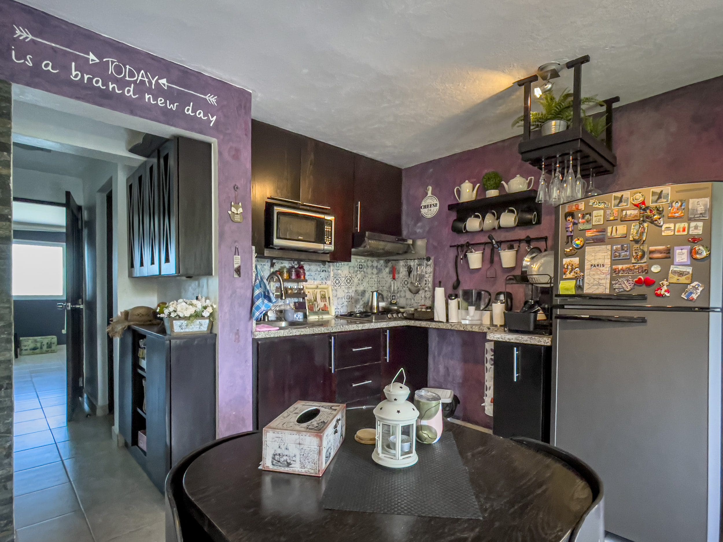 buyDRproperty Cozy kitchen with dark cabinets, microwave, and refrigerator. "Today is a brand new day" sign. Sosua Real Estate
