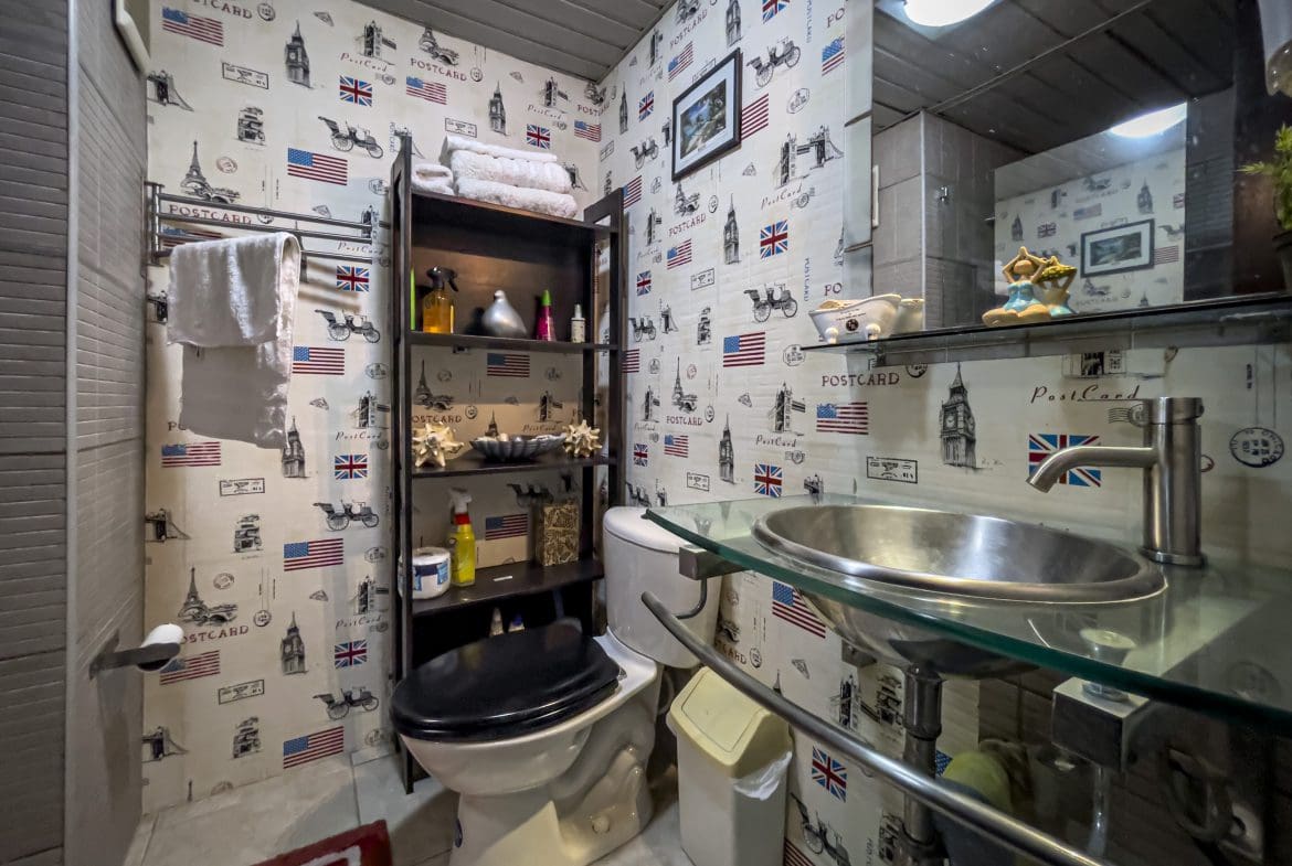 buyDRproperty Small bathroom with themed wallpaper. Sink, toilet and shelf with towels. Sosua Real Estate