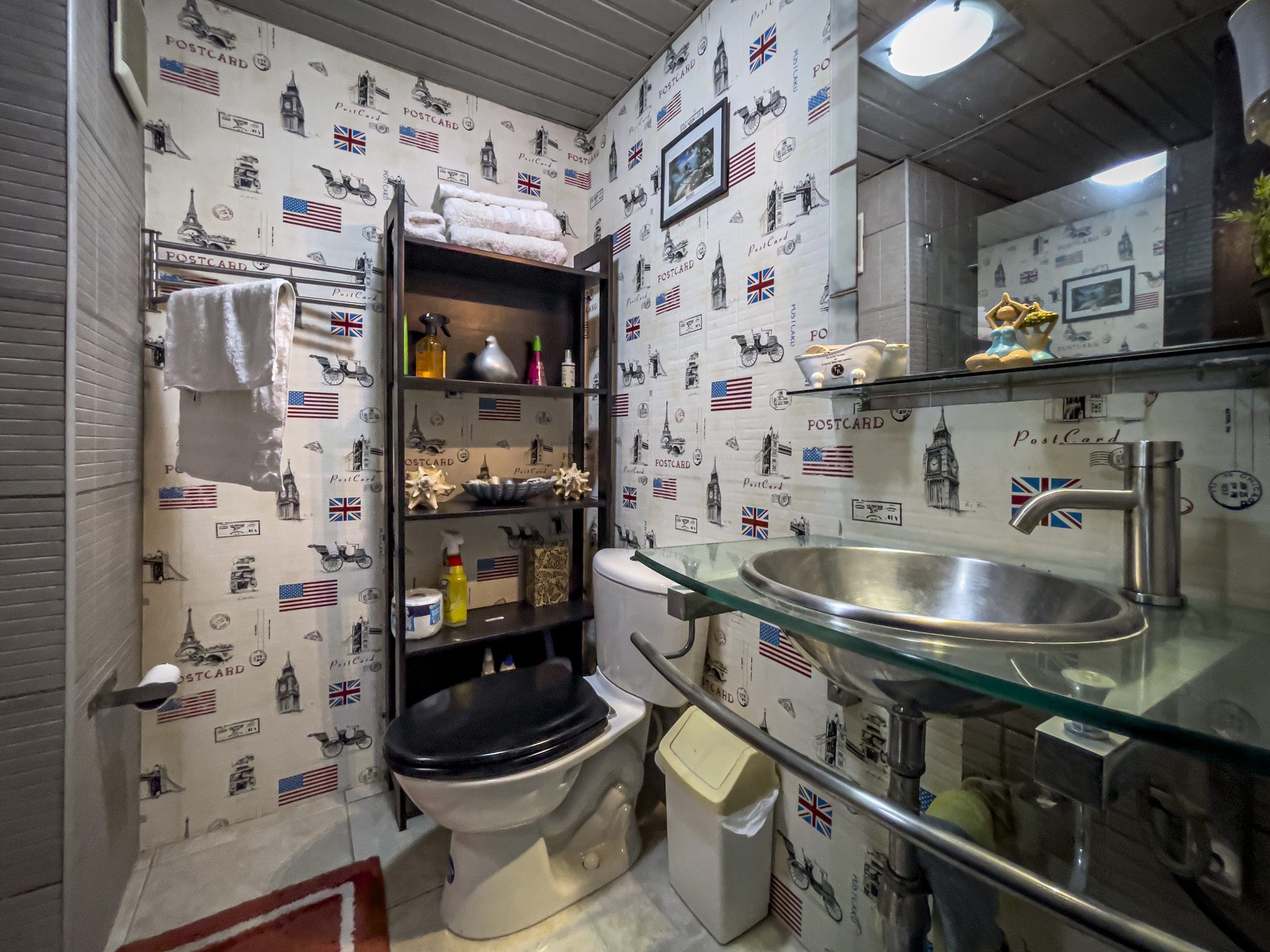 buyDRproperty Small bathroom with themed wallpaper. Sink, toilet and shelf with towels. Sosua Real Estate