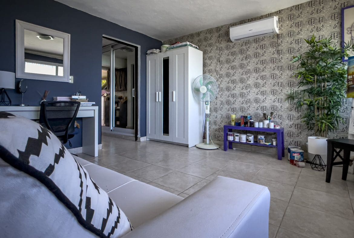buyDRproperty Living room of a 2 bedroom condo in Sosua with white sofa, desk, and patterned wallpaper. Sosua Real Estate