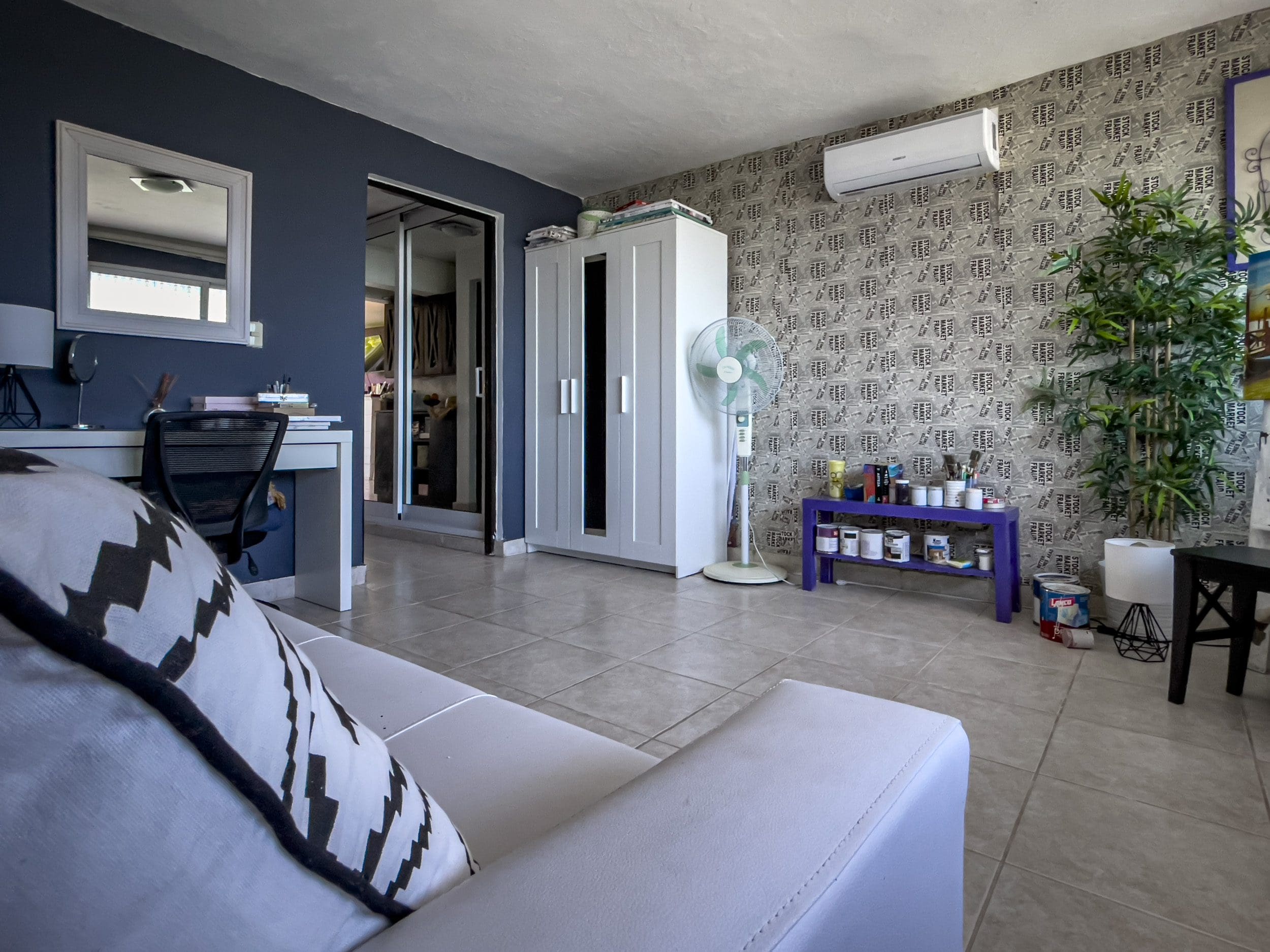 buyDRproperty Living room of a 2 bedroom condo in Sosua with white sofa, desk, and patterned wallpaper. Sosua Real Estate