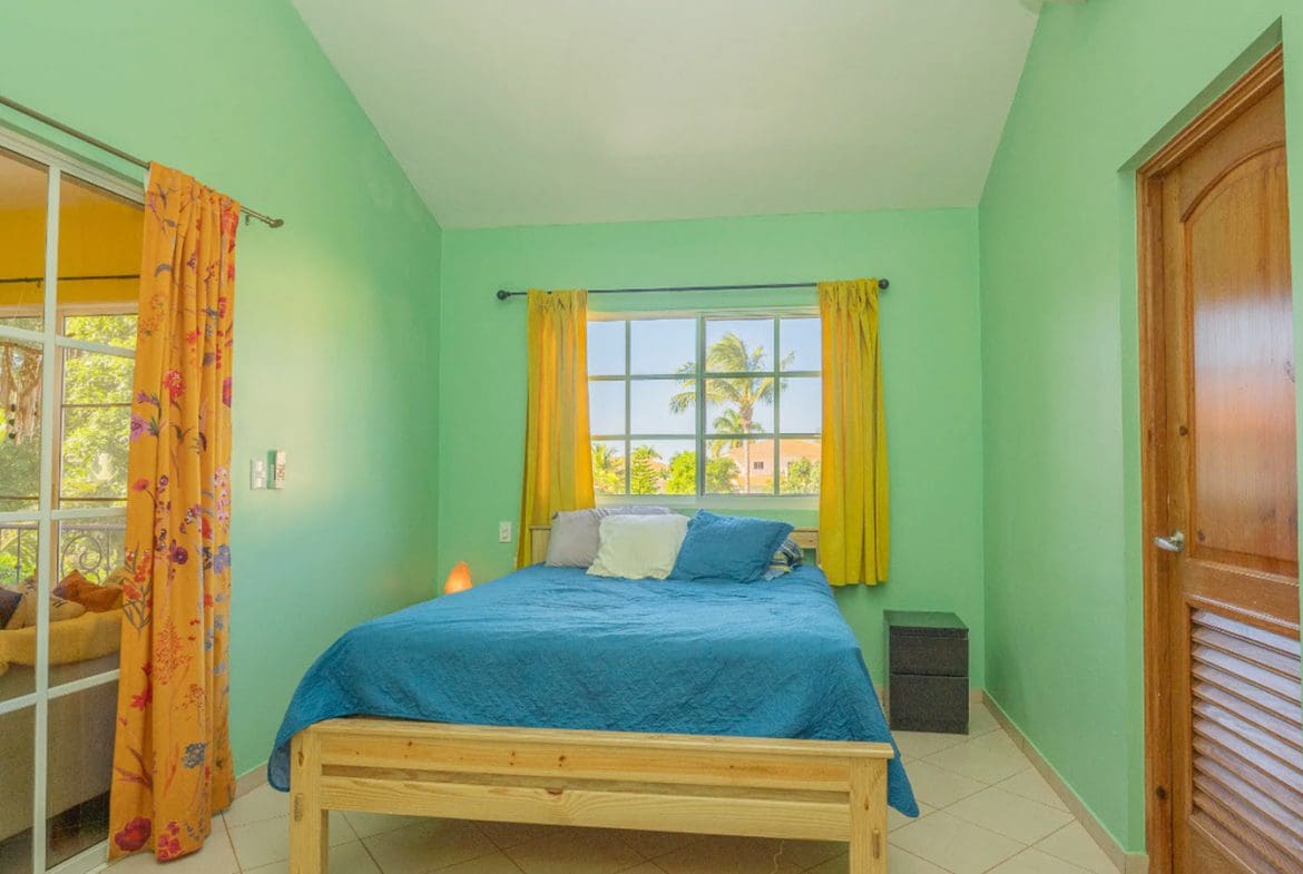 buyDRproperty Bedroom in a Hispaniola Two Unit Villa with blue bedding, yellow curtains, and a wooden door. Sosua Real Estate