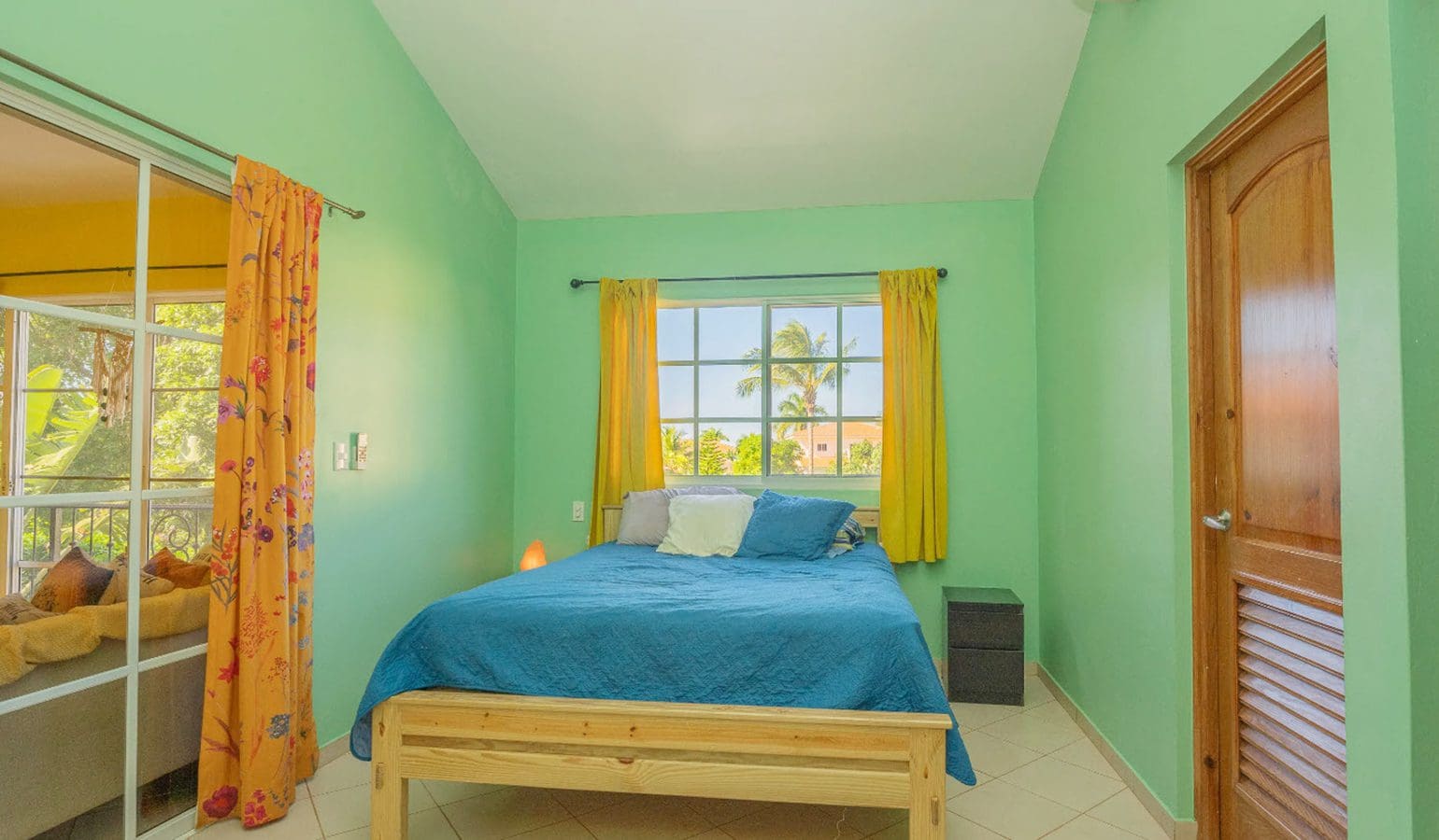 buyDRproperty Bedroom in a Hispaniola Two Unit Villa with blue bedding, yellow curtains, and a wooden door. Sosua Real Estate