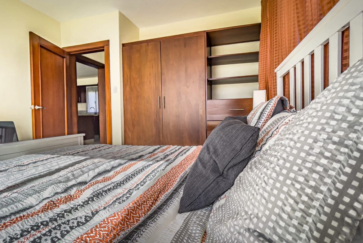 buyDRproperty Bedroom in a 2 Bedroom Villa For Sale, featuring a bed with patterned bedding and a large wardrobe. Sosua Real Estate