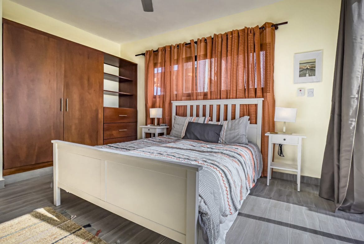 buyDRproperty Bedroom in a 2 Bedroom Villa For Sale with white bed and orange curtains Sosua Real Estate