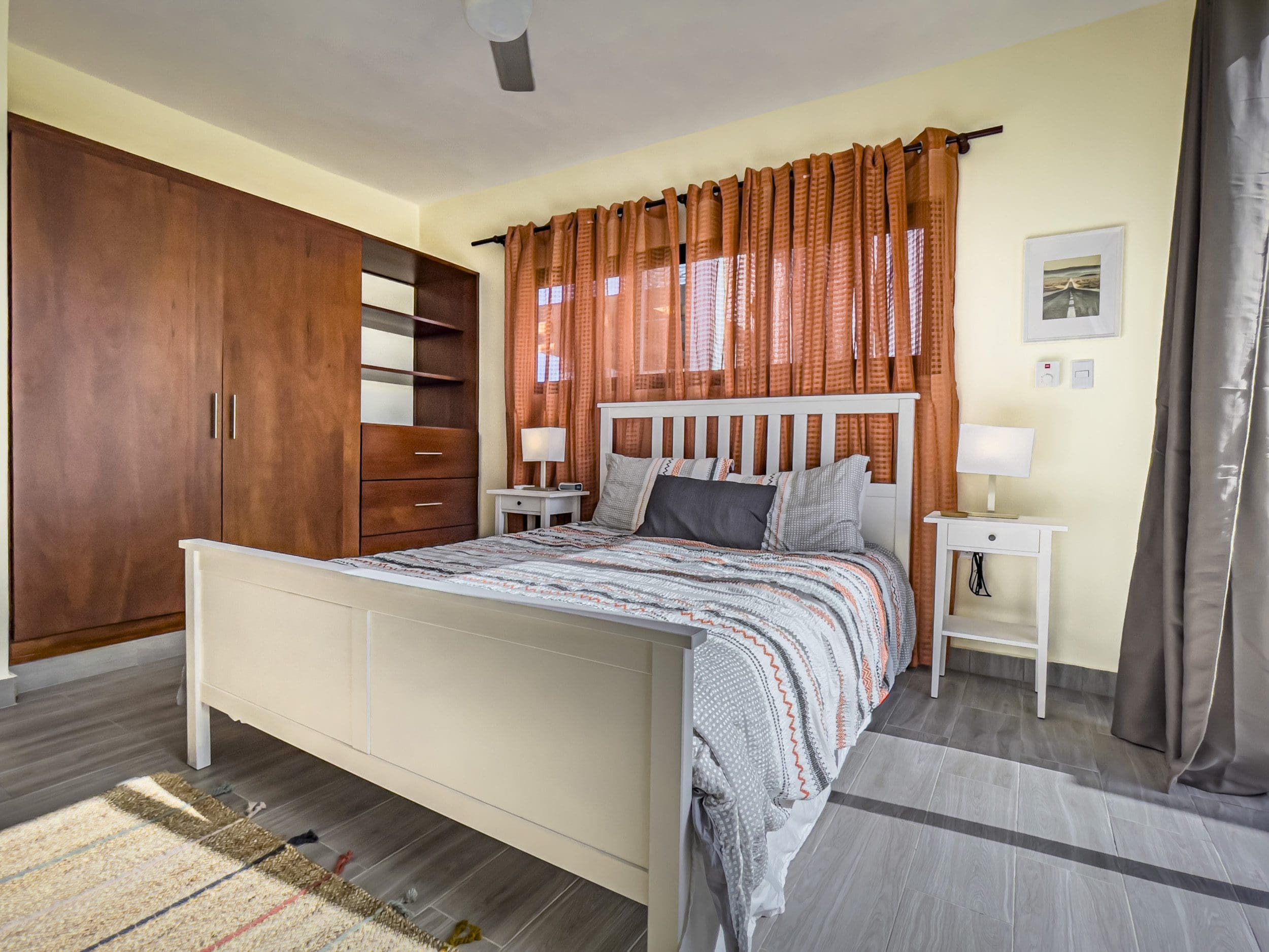 buyDRproperty Bedroom in a 2 Bedroom Villa For Sale with white bed and orange curtains Sosua Real Estate