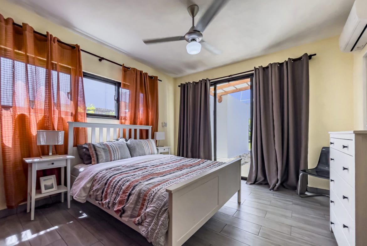 buyDRproperty Bedroom of a 2 Bedroom Villa For Sale with orange curtains, white bed, and sliding door. Sosua Real Estate