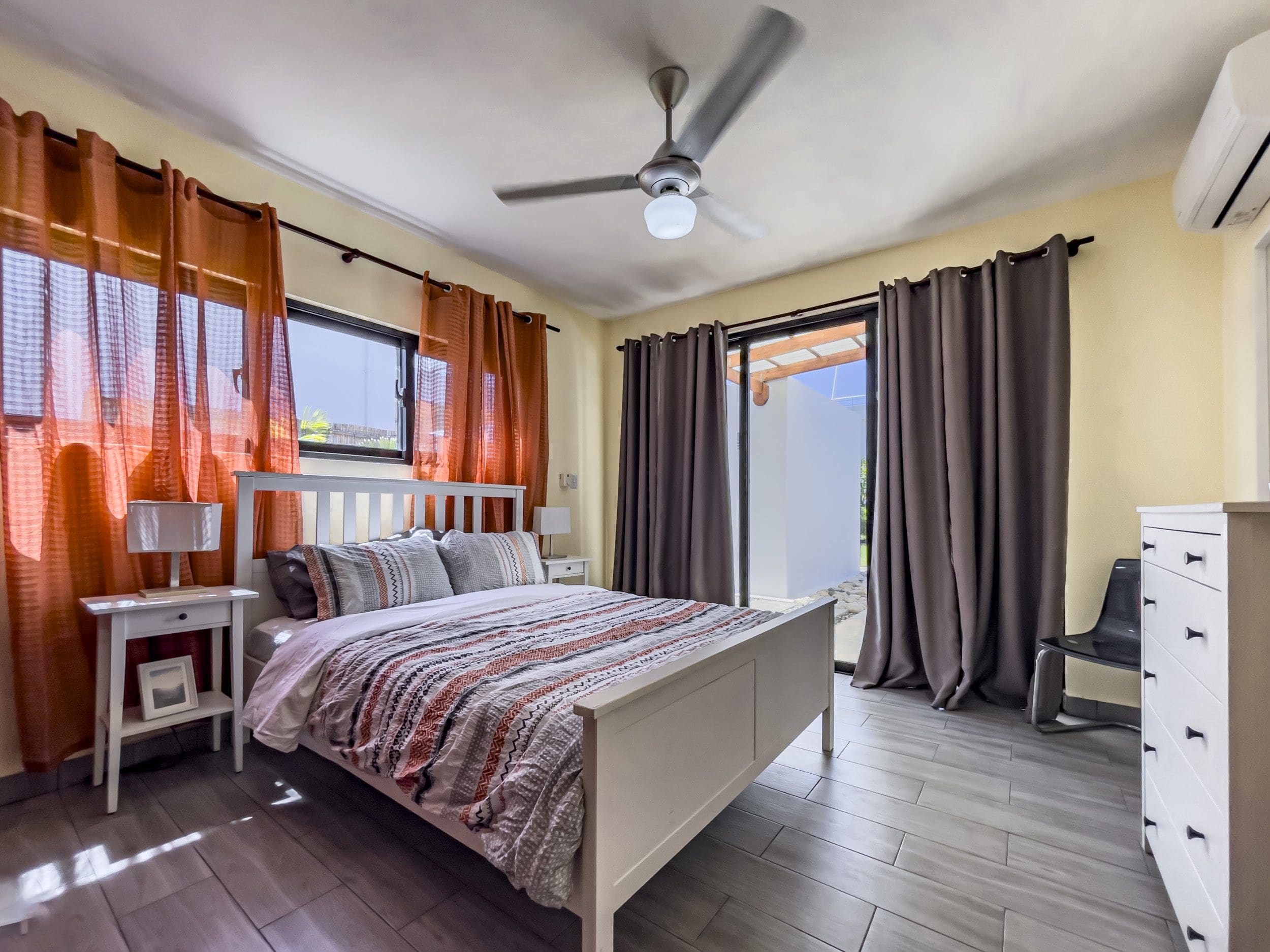 buyDRproperty Bedroom of a 2 Bedroom Villa For Sale with orange curtains, white bed, and sliding door. Sosua Real Estate