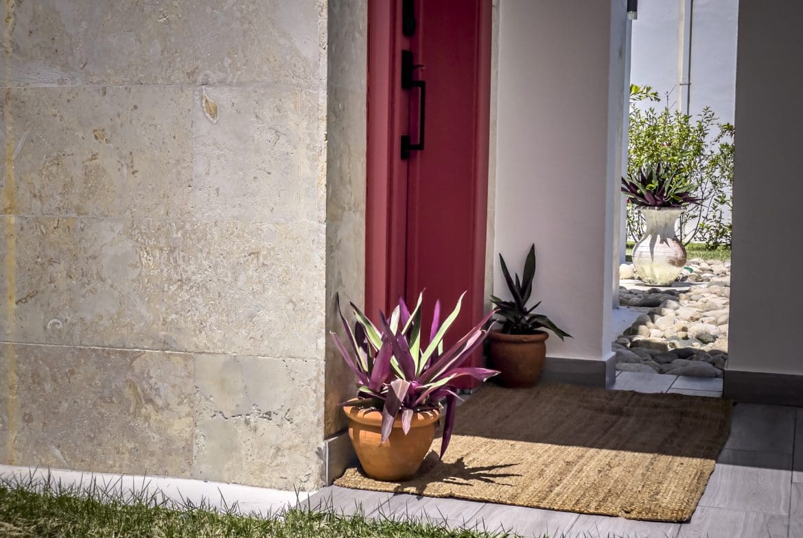 buyDRproperty Entrance of a 2 bedroom villa for sale with colorful plants and red door. Sosua Real Estate
