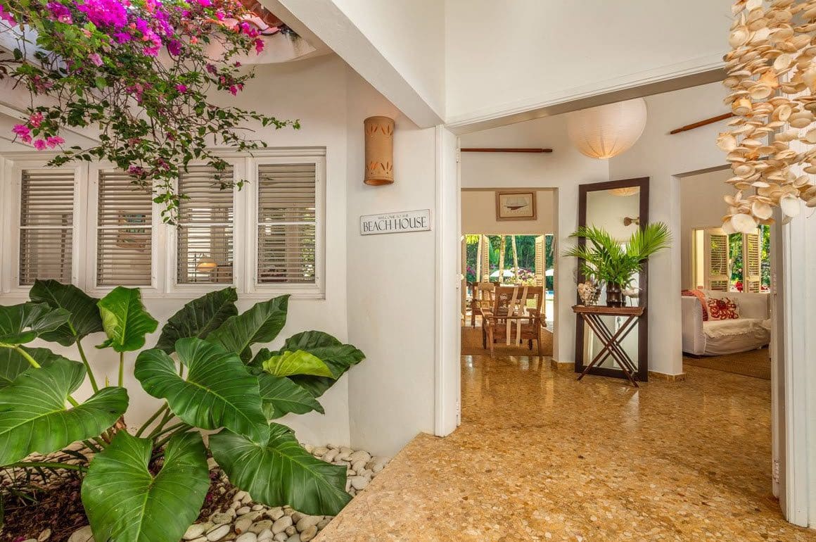 buyDRproperty Beach house entrance with lush greenery and "Beach House" sign. Sosua Real Estate
