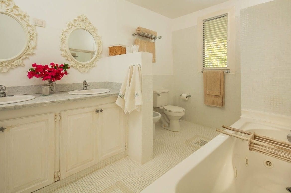 buyDRproperty Bright white bathroom with double vanity, floral mirrors, and a jacuzzi tub. Sosua Real Estate