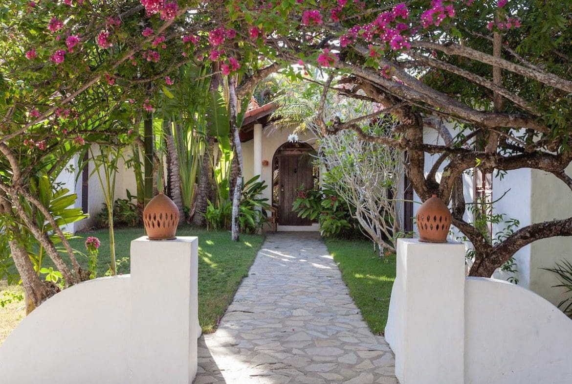 buyDRproperty Stone pathway leading to the entrance of a Sea Horse Ranch Villa, framed by flowering trees. Sosua Real Estate