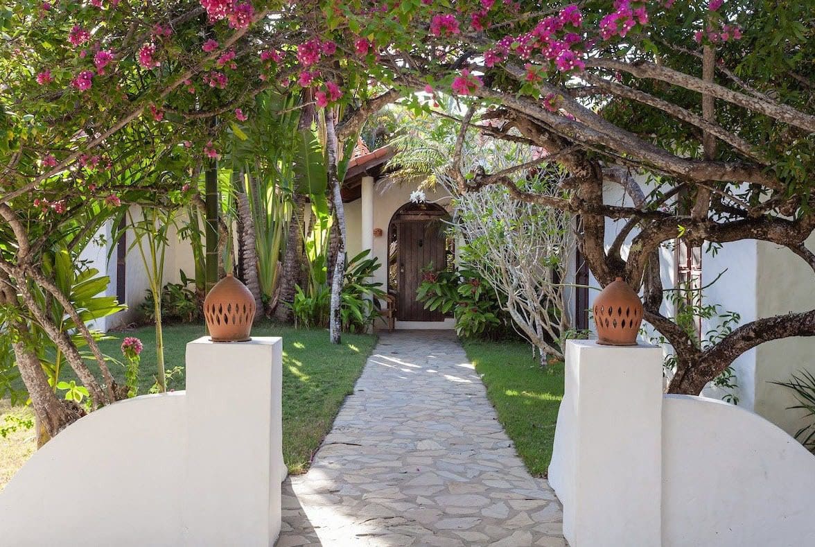 buyDRproperty Stone pathway leading to the entrance of a Sea Horse Ranch Villa, framed by flowering trees. Sosua Real Estate