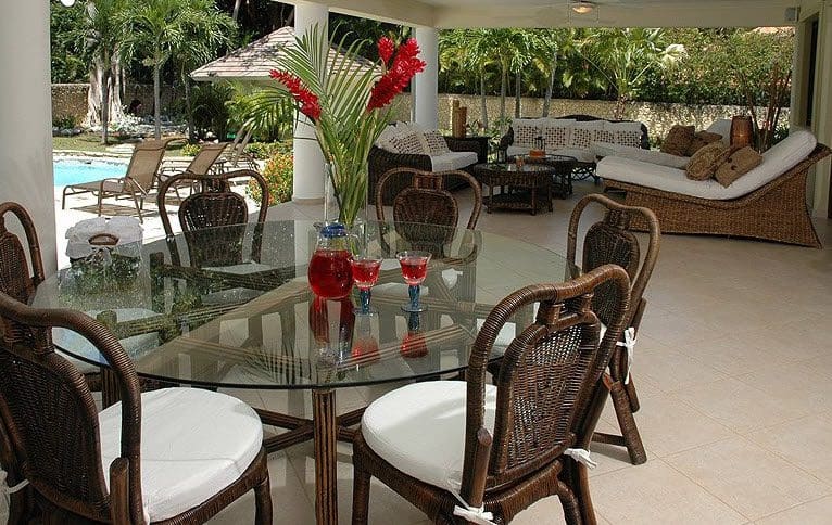 buyDRproperty Outdoor dining area at Beautiful VILLA BRILLANTE: glass table, woven chairs, and pool view. Sosua Real Estate
