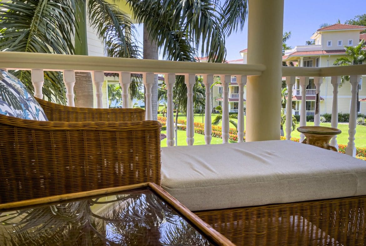 buyDRproperty Relaxing balcony view at a resort, wicker furniture, palm trees, and building in the background. Sosua Real Estate