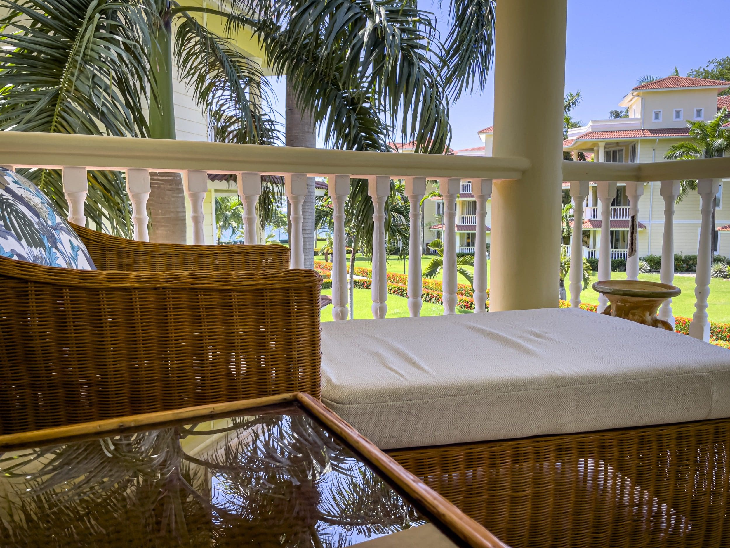 buyDRproperty Relaxing balcony view at a resort, wicker furniture, palm trees, and building in the background. Sosua Real Estate