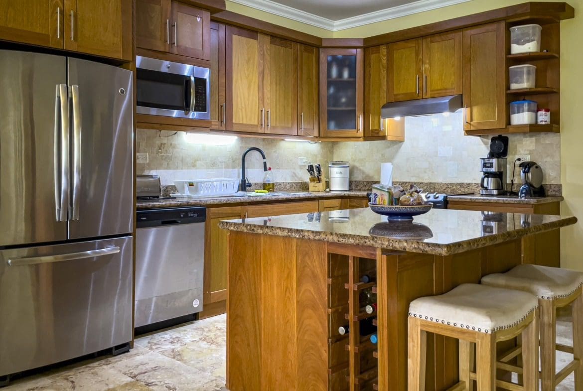 buyDRproperty Modern kitchen with stainless steel appliances, wooden cabinets, and an island with wine storage and stools. Sosua Real Estate