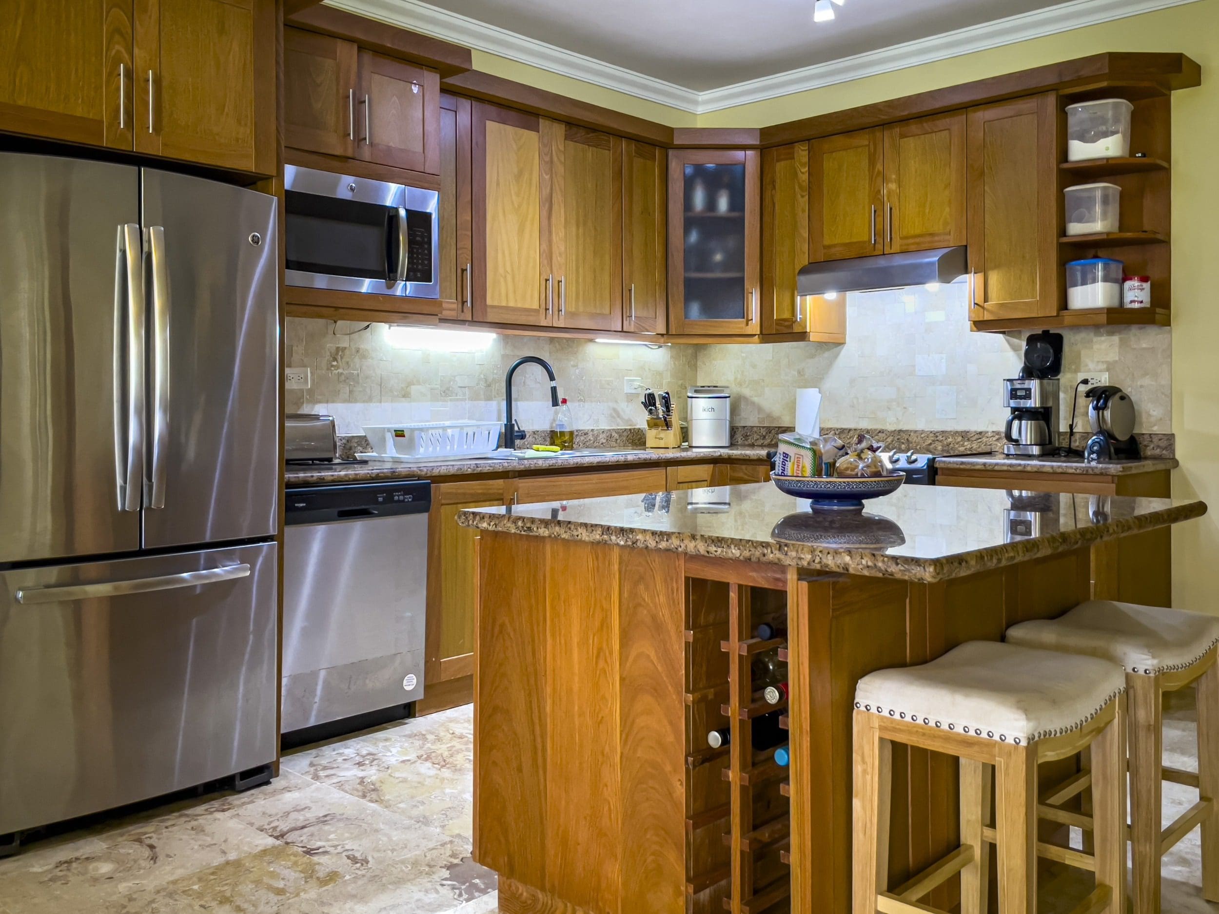 buyDRproperty Modern kitchen with stainless steel appliances, wooden cabinets, and an island with wine storage and stools. Sosua Real Estate