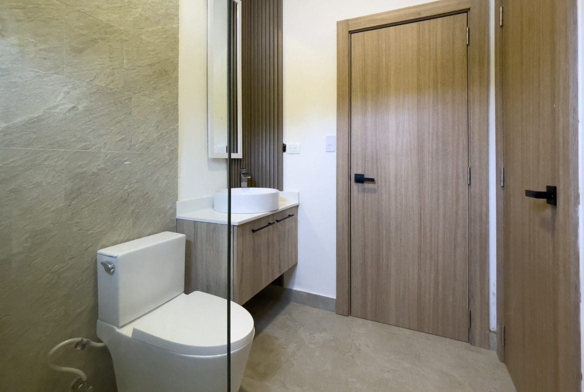 buyDRproperty Modern bathroom with toilet, sink, and wood doors in a Sosua Hills villa for sale. Sosua Real Estate