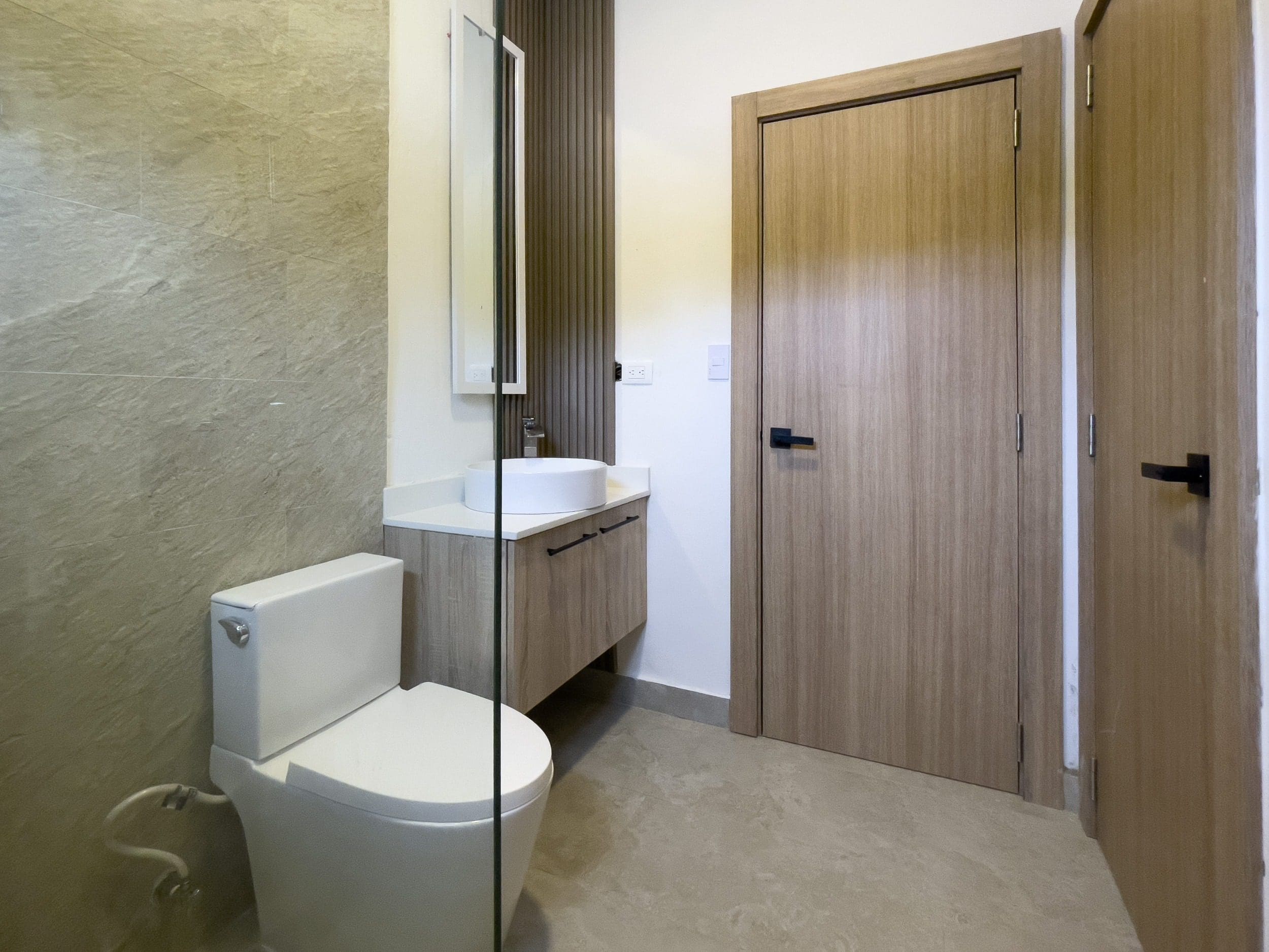 buyDRproperty Modern bathroom with toilet, sink, and wood doors in a Sosua Hills villa for sale. Sosua Real Estate