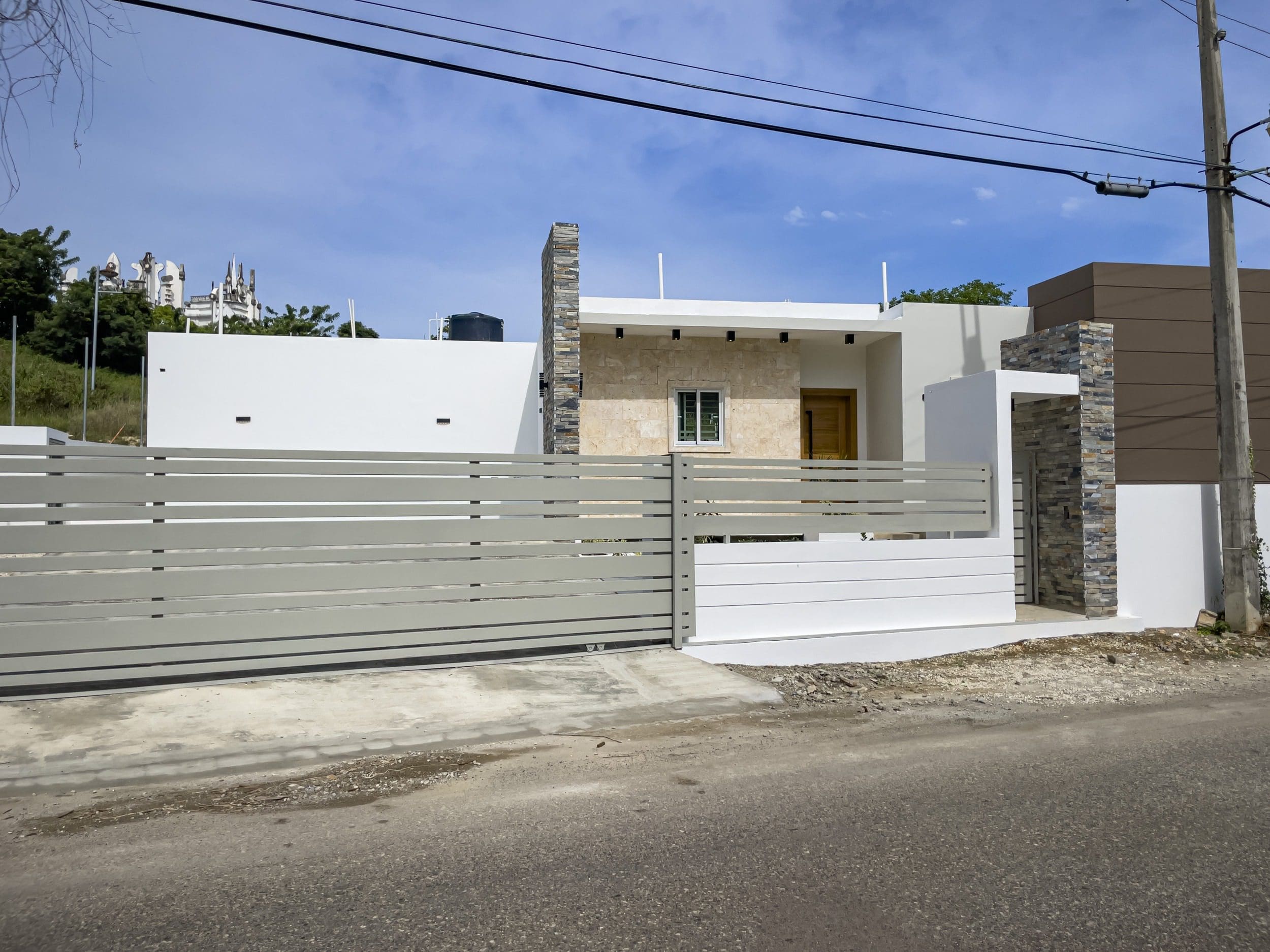buyDRproperty Modern villa for sale in Sosua Hills with a gray gate and stone facade. Sosua Real Estate