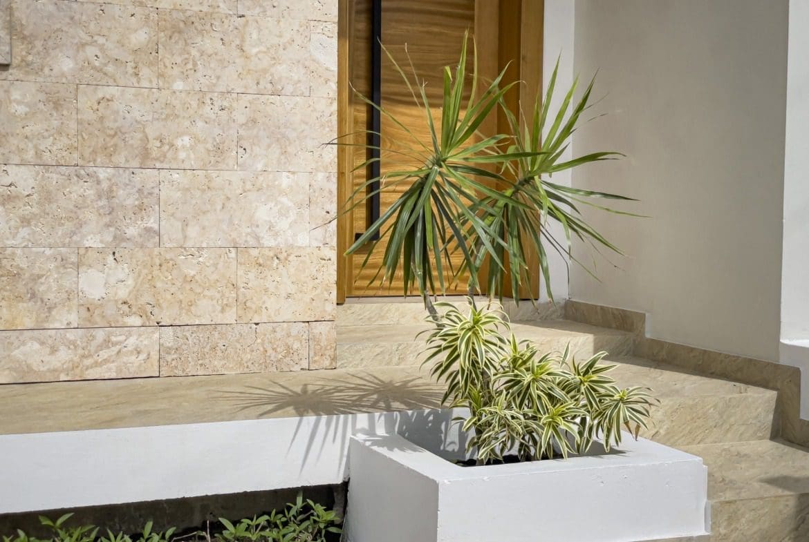 buyDRproperty Villa for sale exterior with wooden door, stone wall and decorative plants. Sosua Real Estate