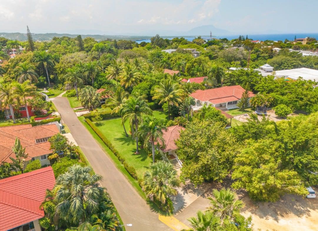 buyDRproperty Aerial view of a tropical residential area with houses featuring red tile roofs and lush green vegetation. Sosua Real Estate