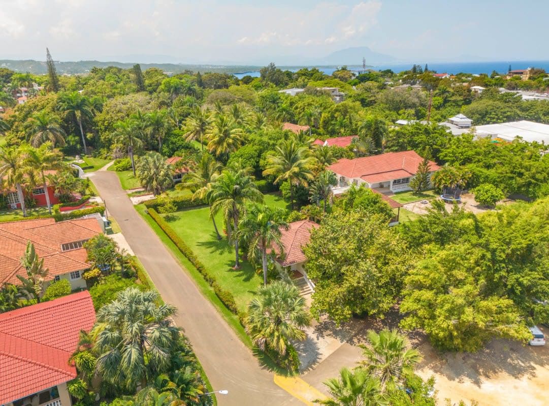 buyDRproperty Aerial view of a tropical residential area with houses featuring red tile roofs and lush green vegetation. Sosua Real Estate