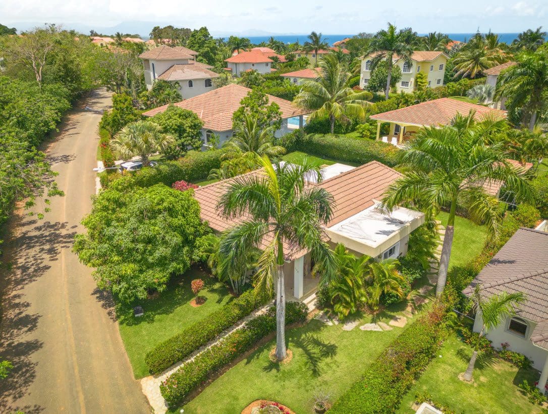buyDRproperty Aerial view of a beautiful villa in a gated community with palm trees and lush landscaping. Sosua Real Estate