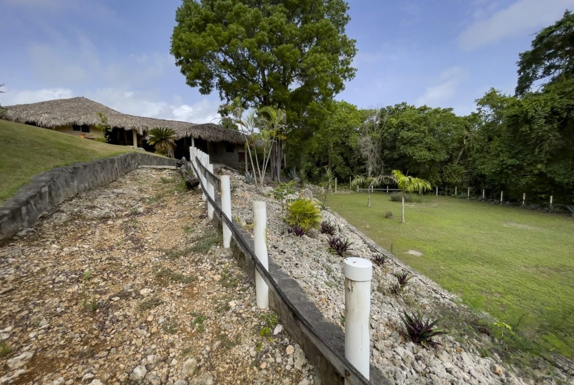 buyDRproperty Pathway leading to a tropical resort with thatched roofs, surrounded by lush greenery and blue sky. Sosua Real Estate