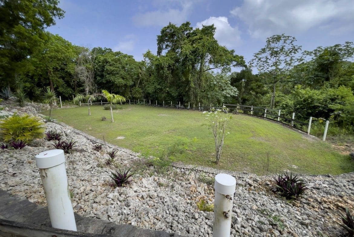 buyDRproperty Grassy building lot surrounded by trees and fence with rocky foreground. Sosua Real Estate