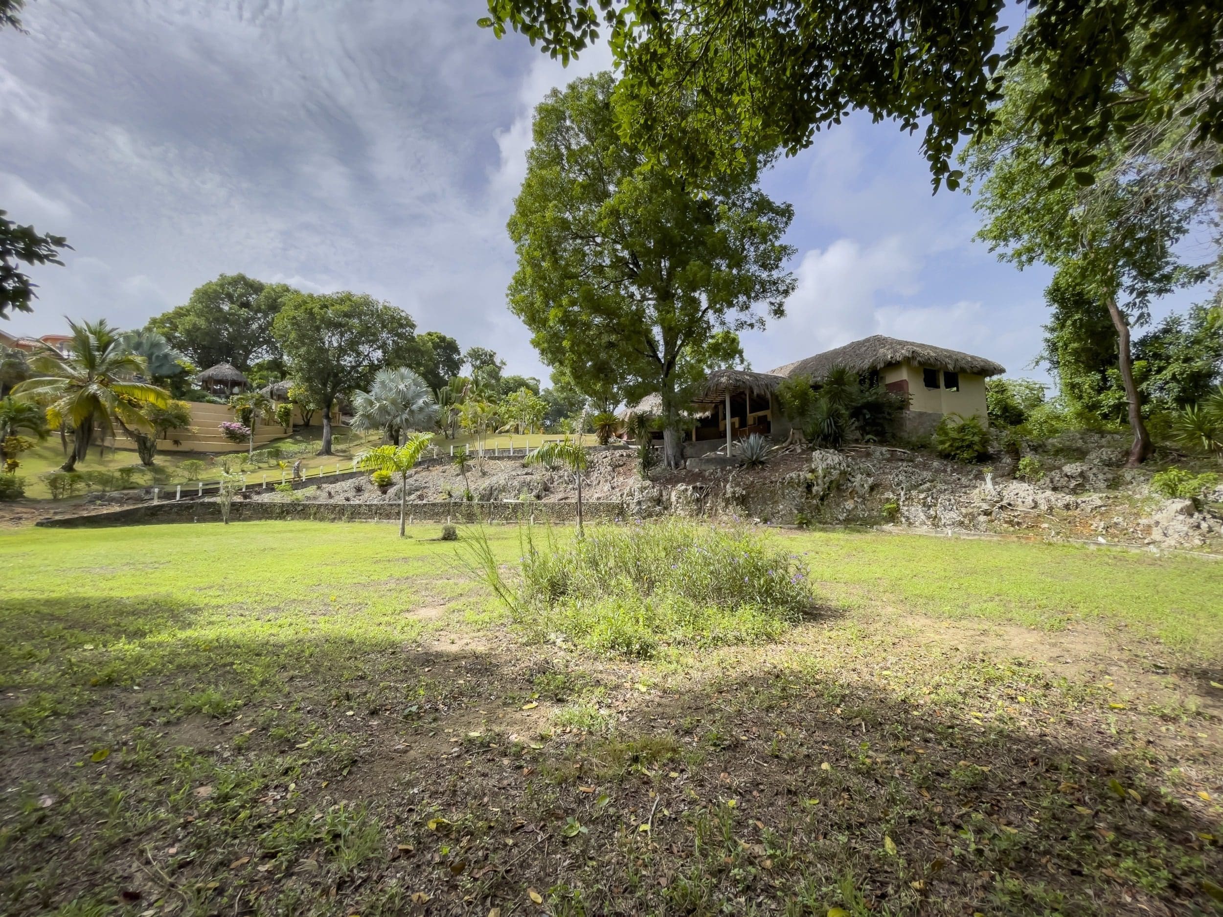 buyDRproperty Tropical building lot with thatched roof structures and lush green grass. Sosua Real Estate