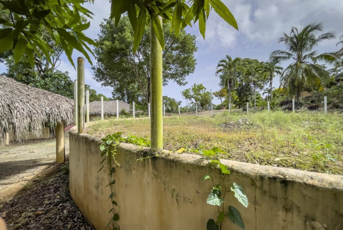 buyDRproperty Building lot with round structure, wall with climbing plants, and thatched roof. Sosua Real Estate