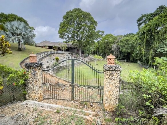 buyDRproperty Gated entrance to building lot with stone pillars, lush landscaping, and thatched roof building. Sosua Real Estate