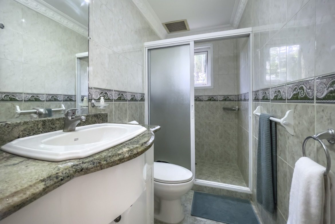 buyDRproperty Bathroom with a white sink and marble countertop. Shower with frosted glass door. Sosua Real Estate