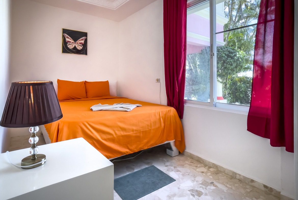 buyDRproperty Bedroom with orange bed, butterfly art, and red curtains. Prime location. Sosua Real Estate