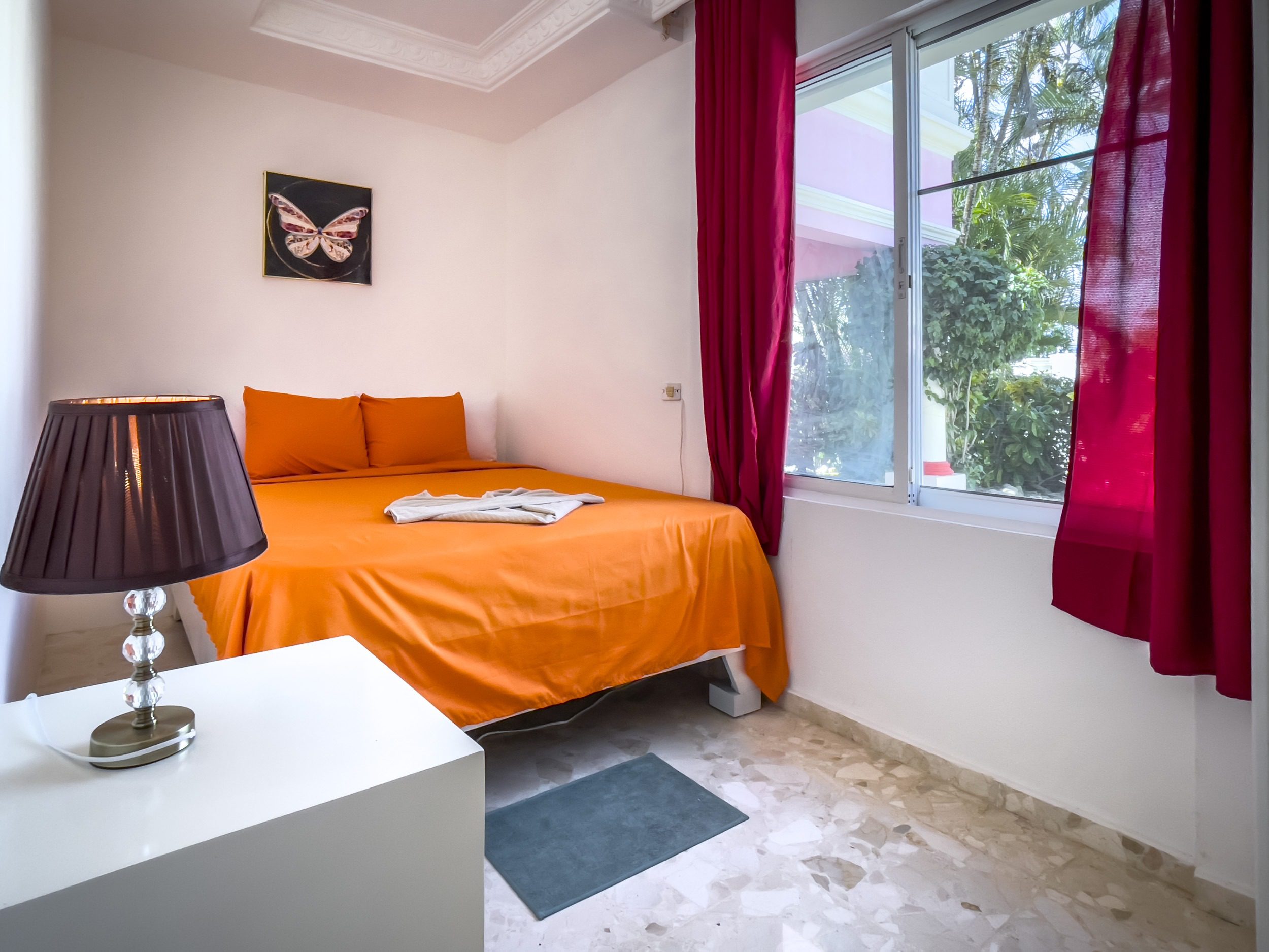 buyDRproperty Bedroom with orange bed, butterfly art, and red curtains. Prime location. Sosua Real Estate
