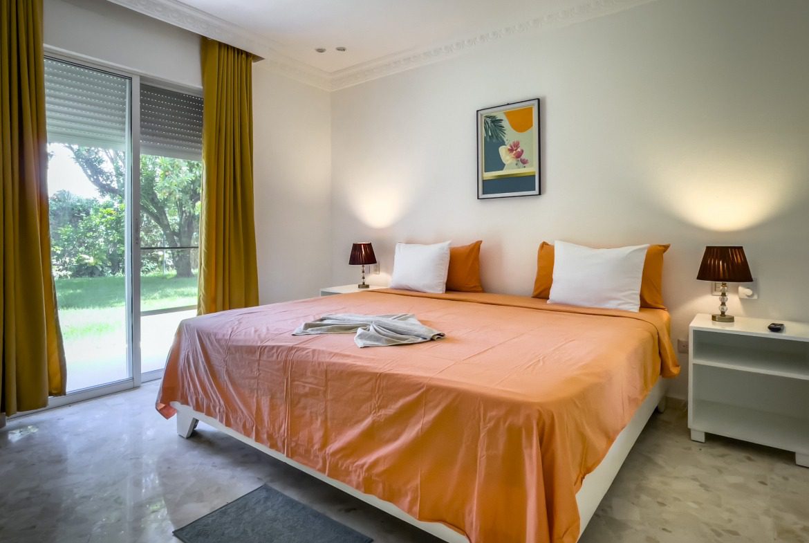 buyDRproperty Bedroom in prime villa for sale near beach with orange bedding, white pillows, and artwork. Sosua Real Estate