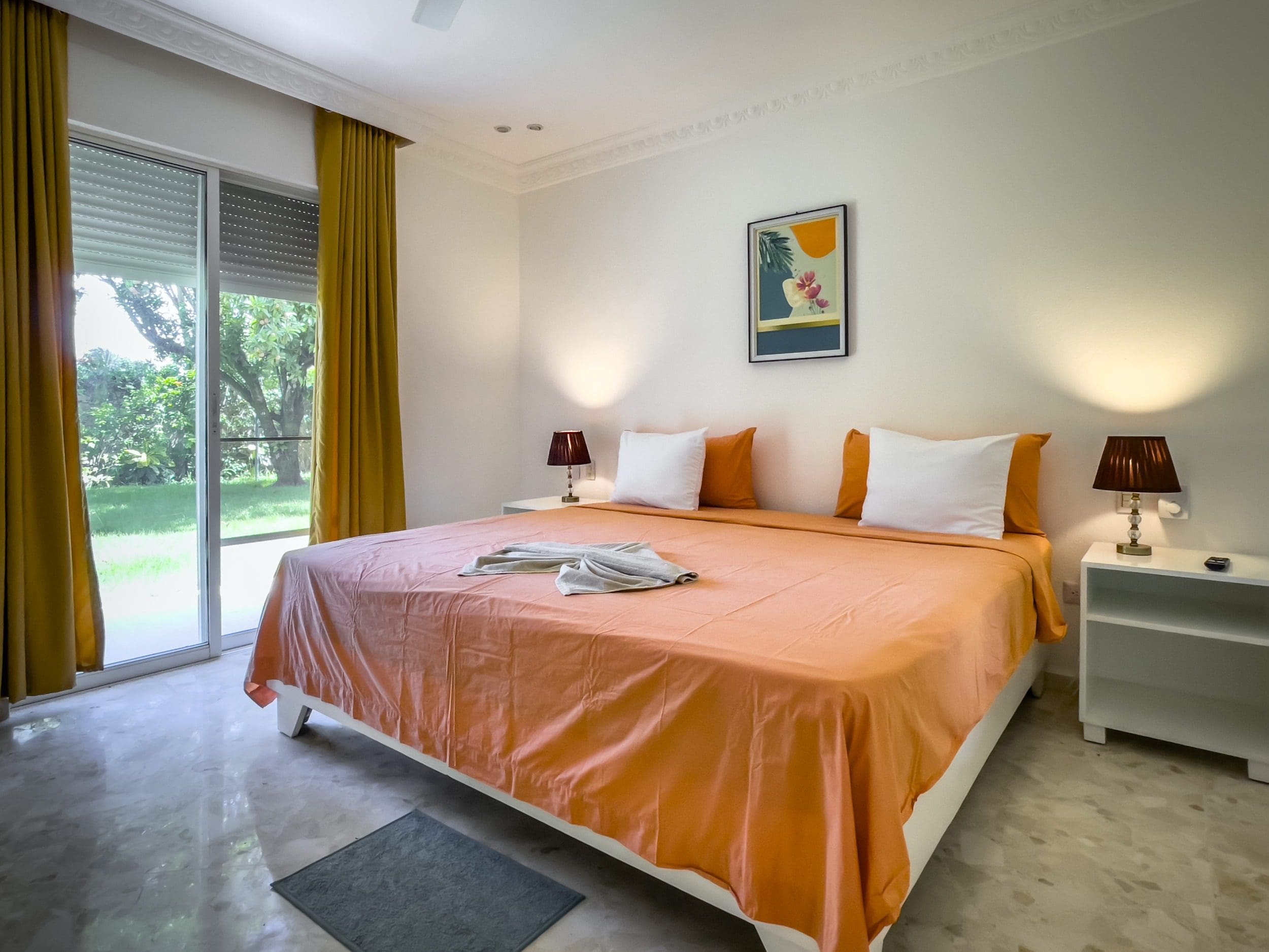 buyDRproperty Bedroom in prime villa for sale near beach with orange bedding, white pillows, and artwork. Sosua Real Estate