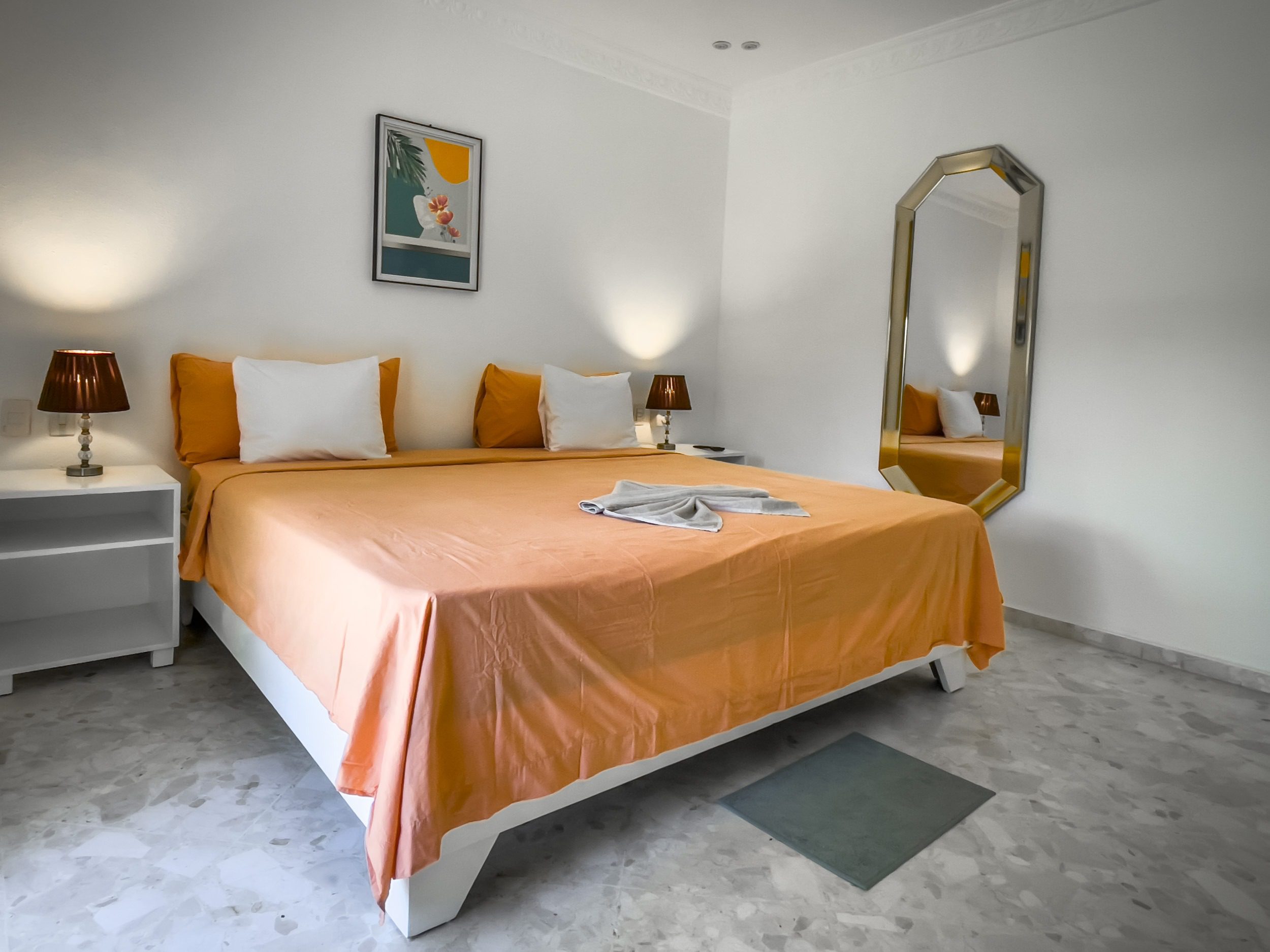 buyDRproperty Modern bedroom with orange bedspread, white pillows, and large mirror; prime villa. Sosua Real Estate