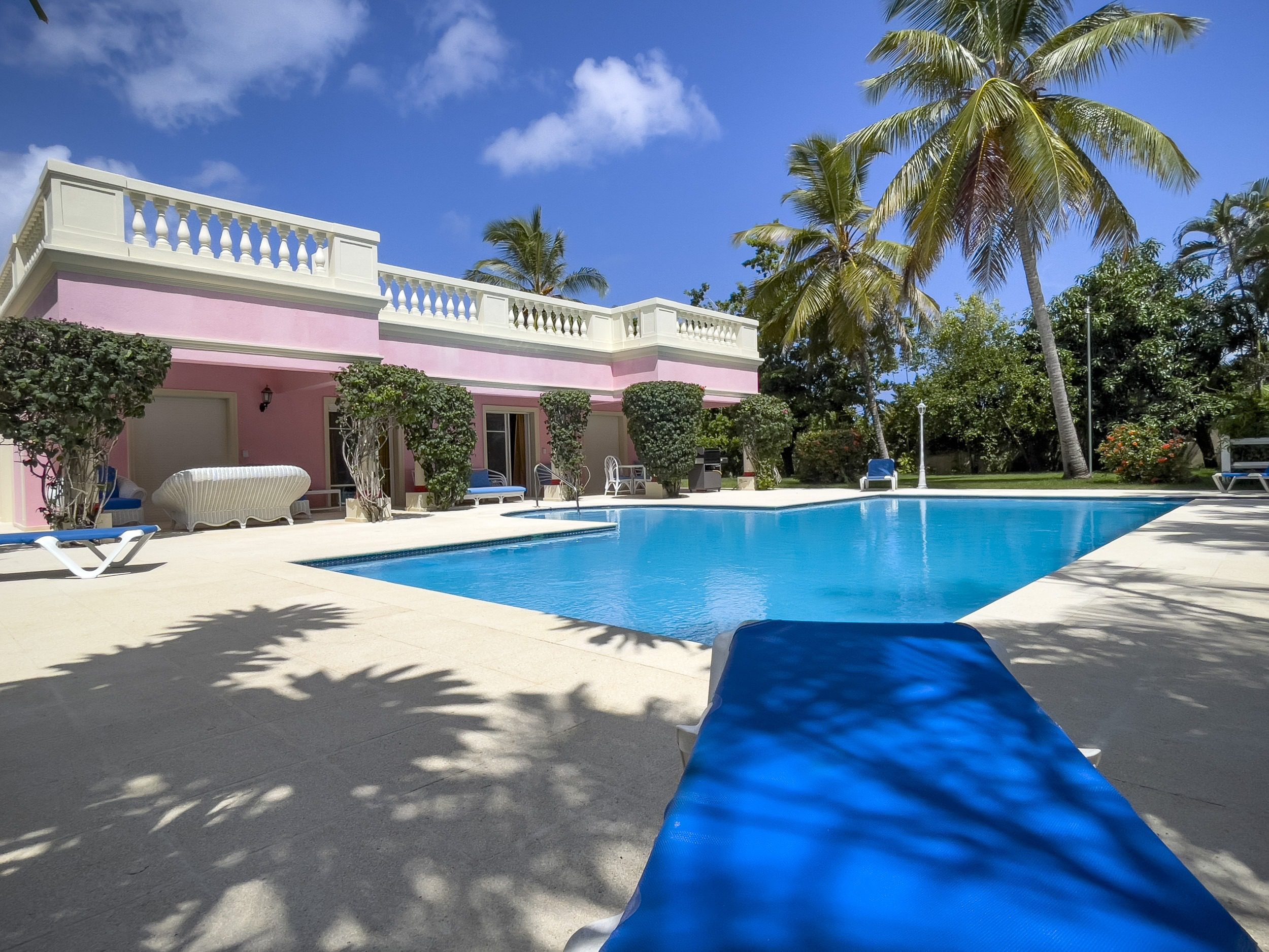 buyDRproperty Prime pink villa with a pool and palm trees under a blue sky. Sosua Real Estate
