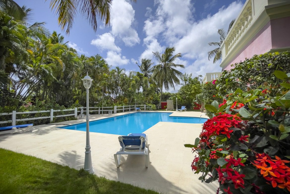buyDRproperty Prime villa with a swimming pool, palm trees, and red flowers under a blue sky. Sosua Real Estate
