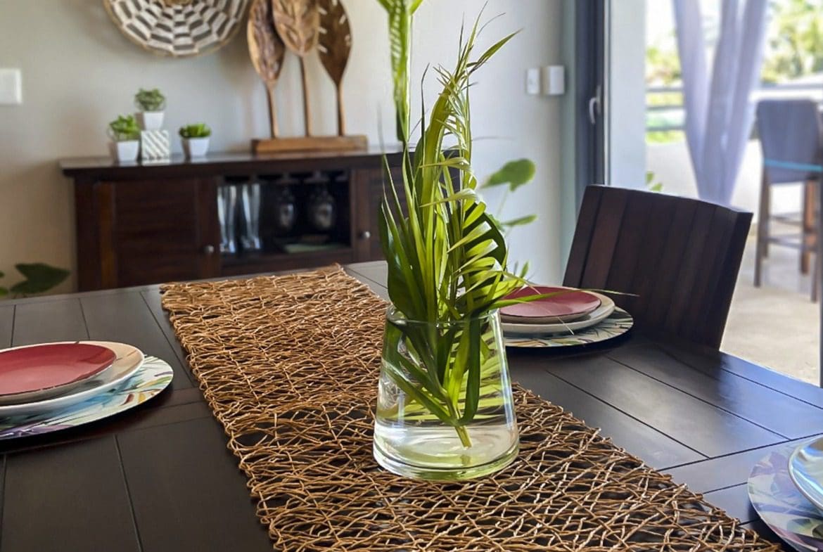 buyDRproperty Dining table set with woven runner, greenery centerpiece, and plates. Interior design. Sosua Real Estate