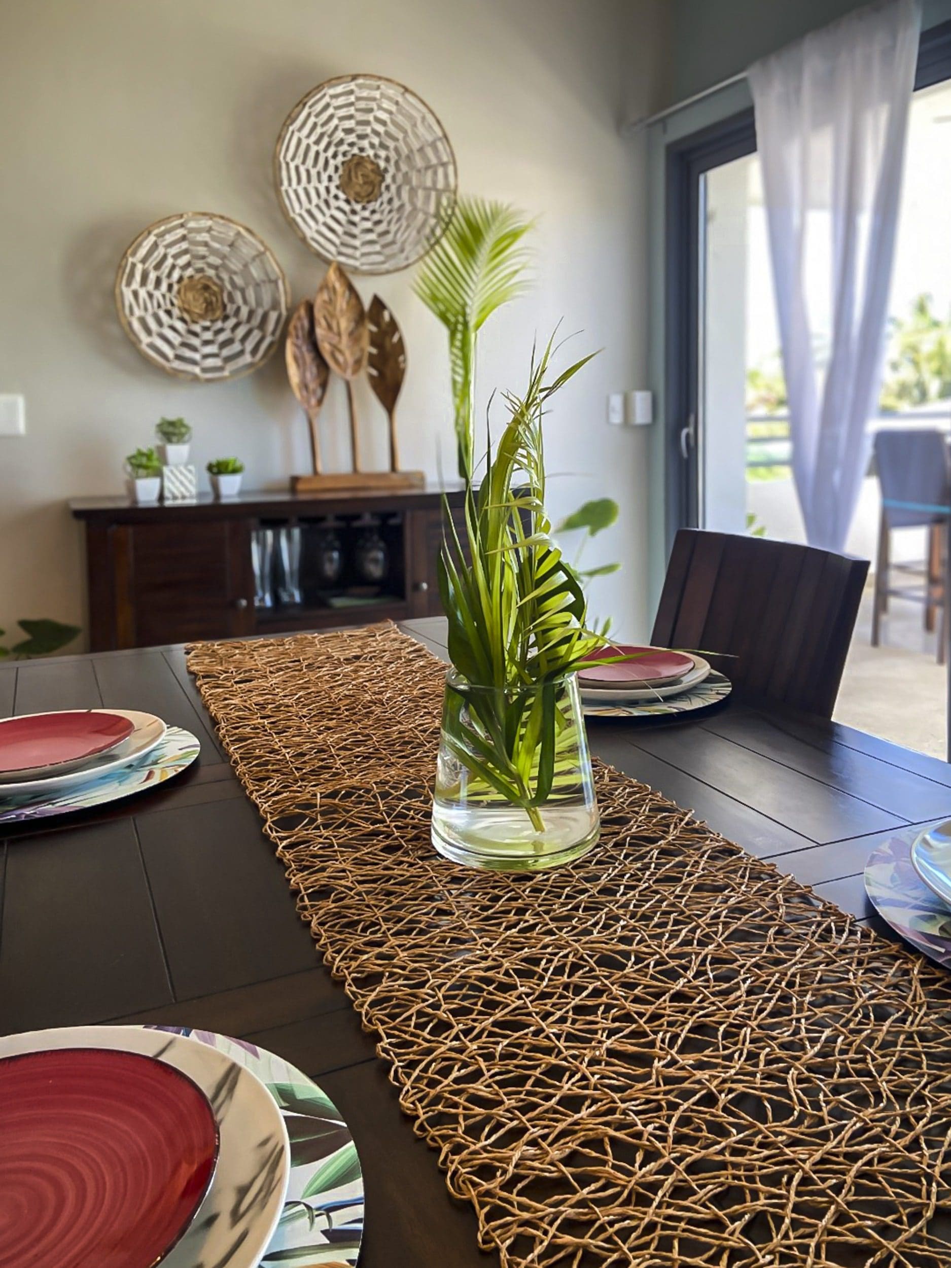 buyDRproperty Dining table set with woven runner, greenery centerpiece, and plates. Interior design. Sosua Real Estate