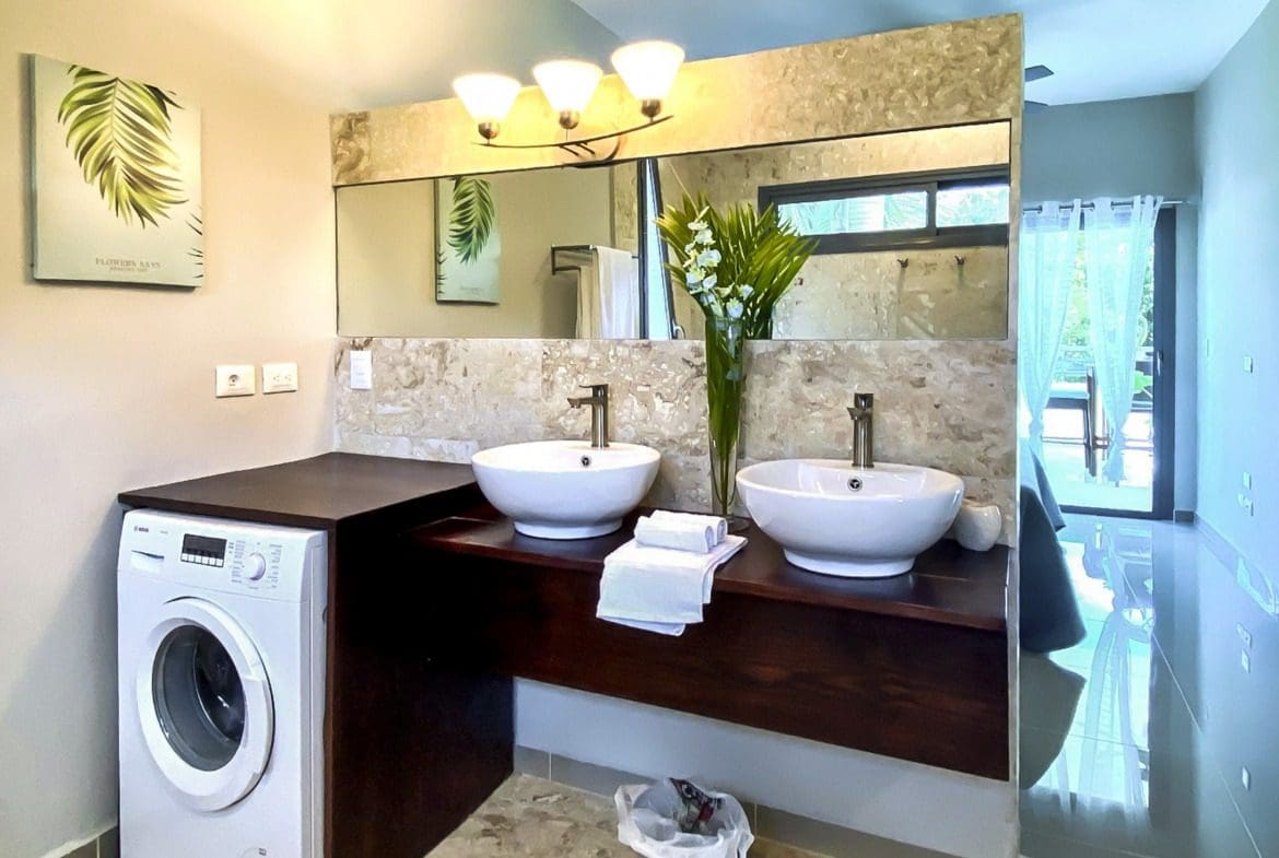 buyDRproperty Modern bathroom with double sinks, washing machine, and balcony access. Sosua Real Estate