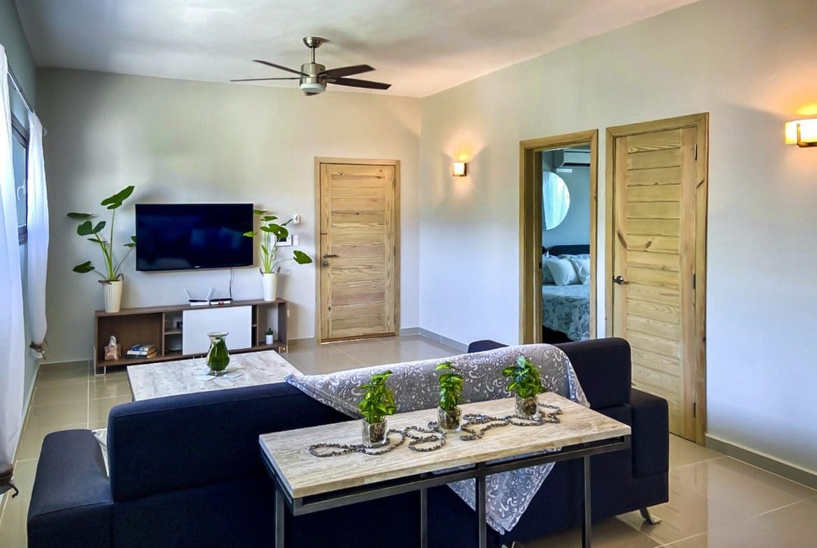 buyDRproperty Modern living room with dark blue sofa, TV, and wooden doors. Potential for sale in ProCab. Sosua Real Estate