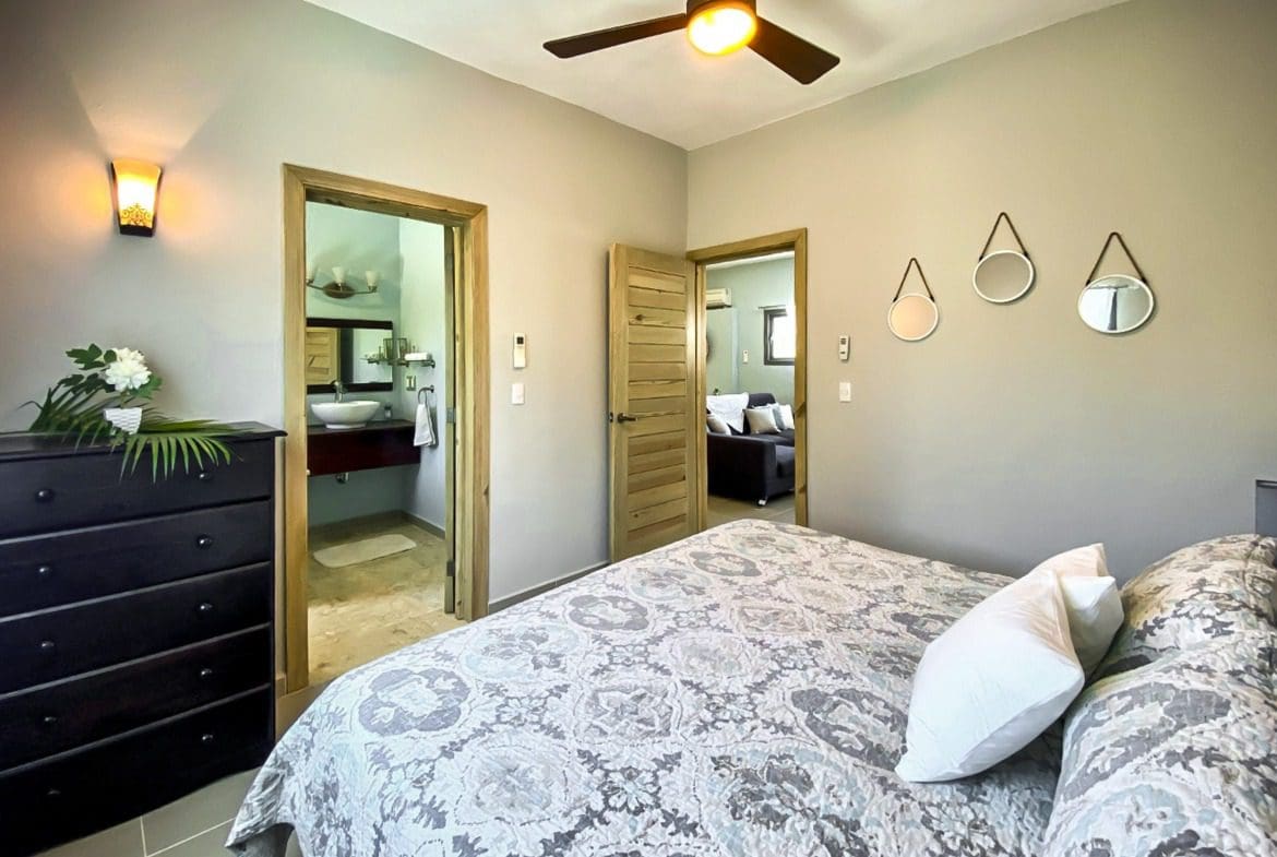 buyDRproperty Bedroom in a ProCab penthouse for sale, featuring a bed, dresser, and bathroom access. Sosua Real Estate