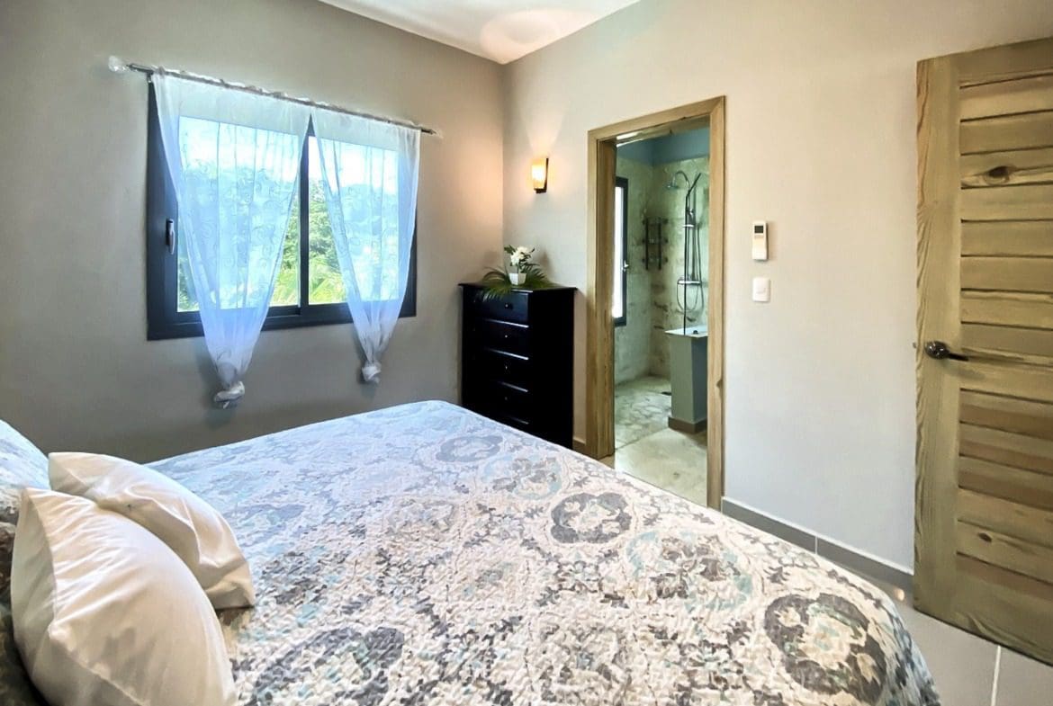 buyDRproperty Bedroom with bed, window, and doorway to bathroom. Modern design. Sosua Real Estate