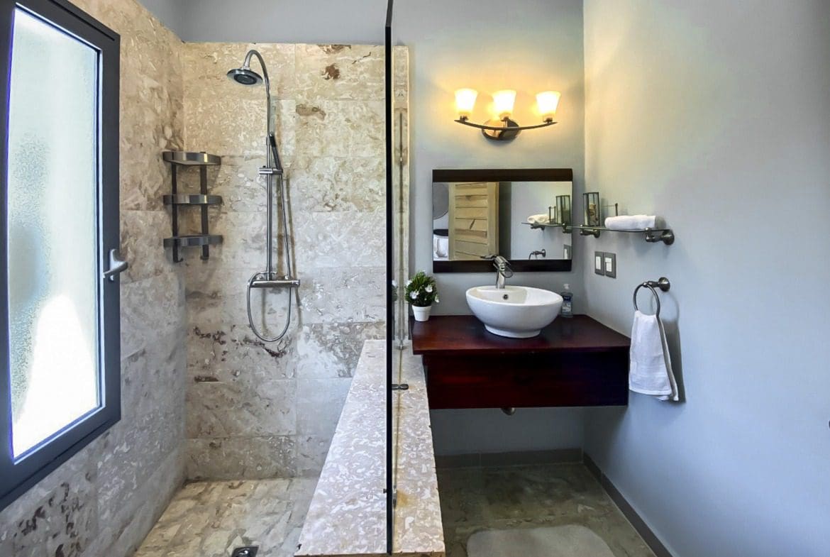 buyDRproperty Modern bathroom with glass shower, floating vanity, and marble tile. Sosua Real Estate